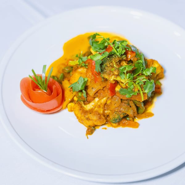 Colorful vegetable curry with broccoli, cauliflower, and peppers, garnished with cilantro and a tomato rose.