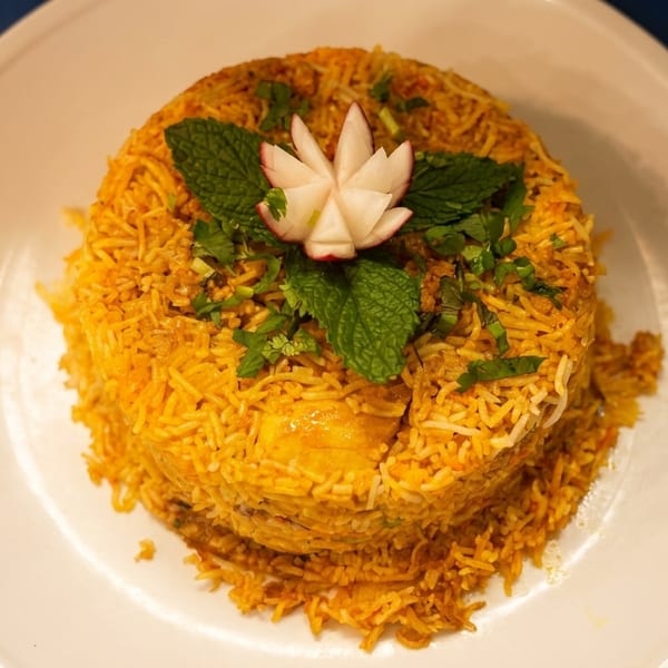 A dome of golden biryani rice, garnished with mint, cilantro, and a carved radish flower.