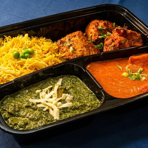 Indian meal prep container with yellow rice, chicken tikka, palak paneer, and butter chicken.