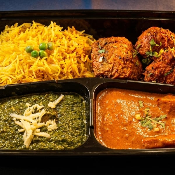 Indian meal prep container with yellow rice, chicken tikka, palak paneer, and butter chicken.