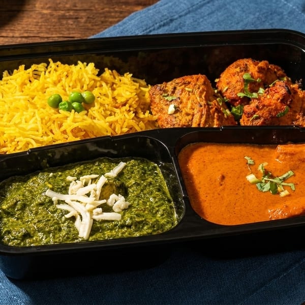 Indian meal in a black tray with yellow rice, chicken tikka, palak paneer, and butter chicken.