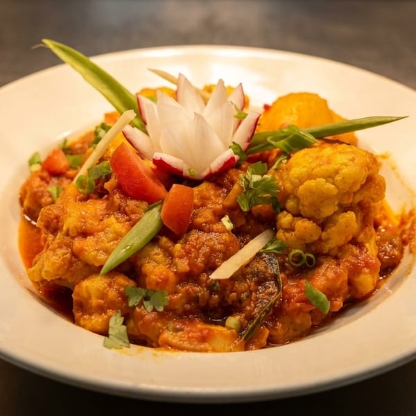 A vibrant Indian curry with cauliflower, tomatoes, and green onions, garnished with a radish flower.